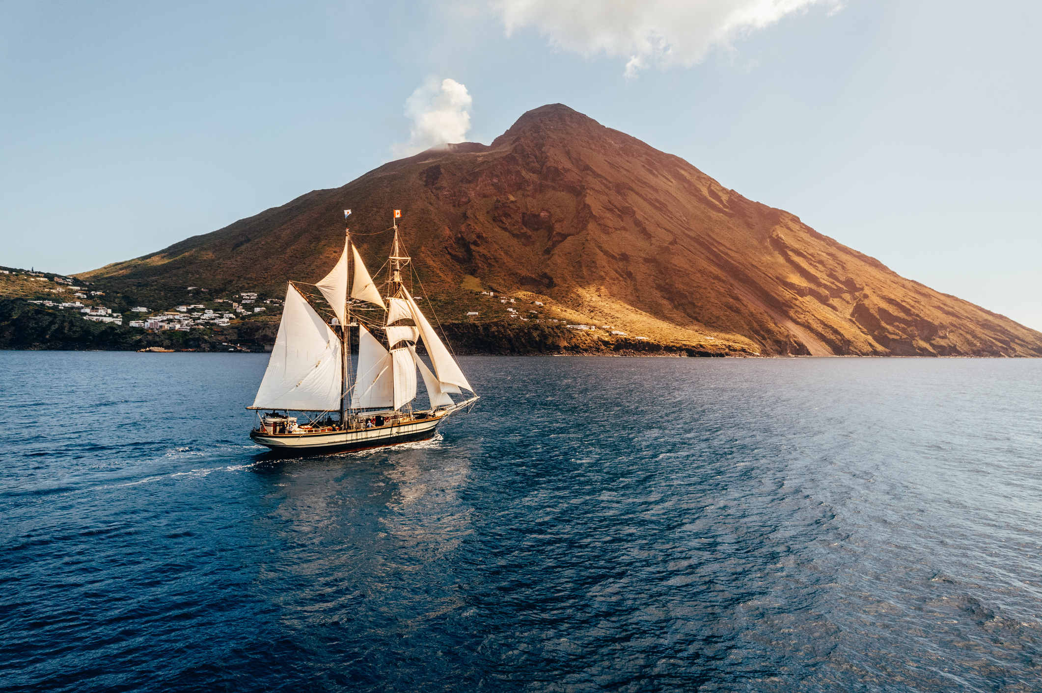 Tall ship sailing past a volcano in Italy during sunset