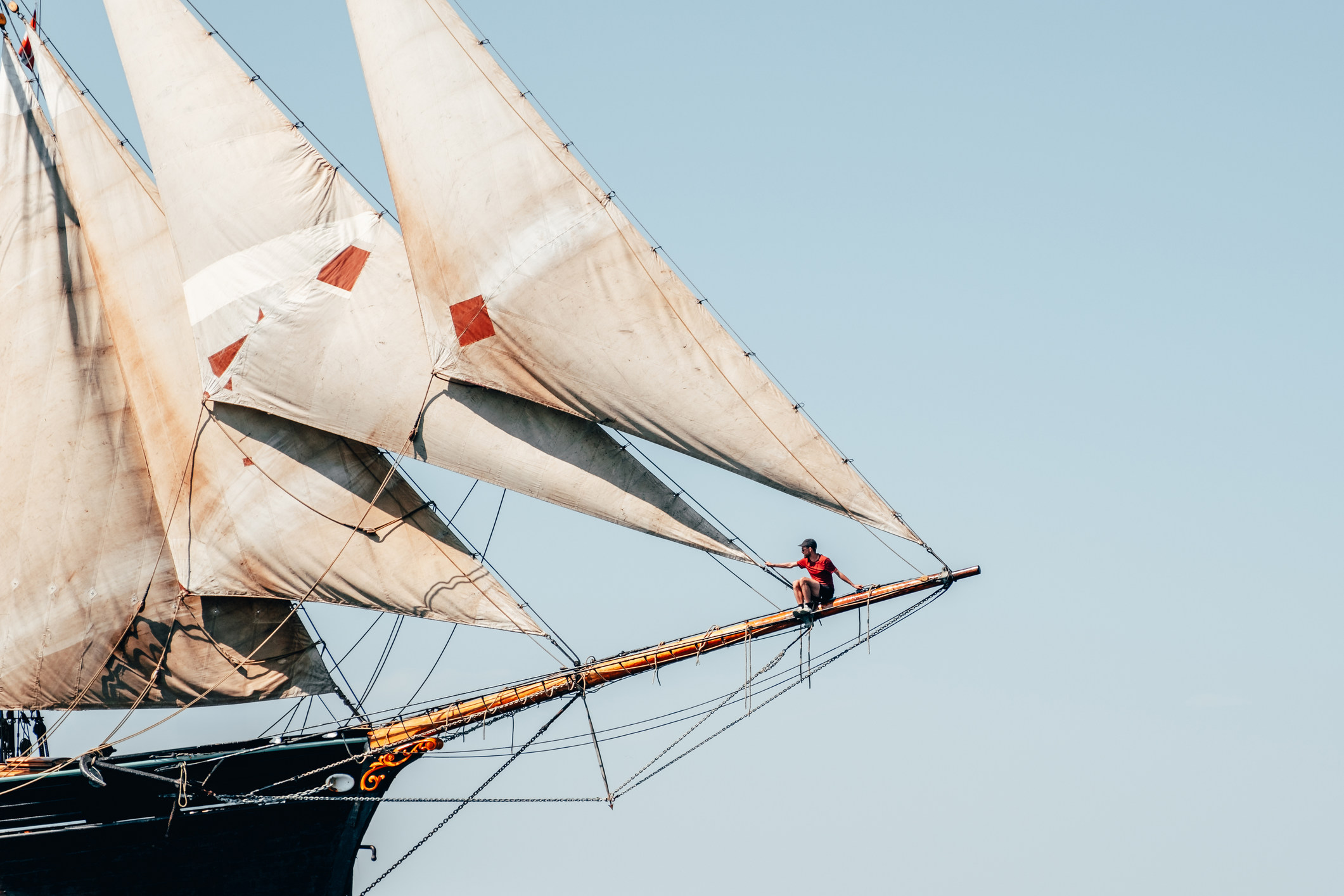 Man sat on the end of the bowsprit of a tall ship at sea