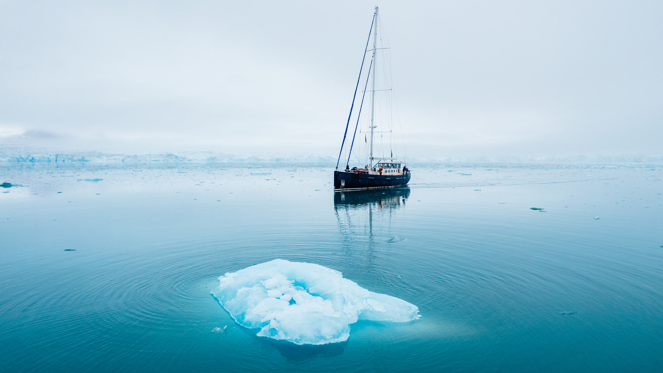 Sailboat in the arctic next to an ice berg