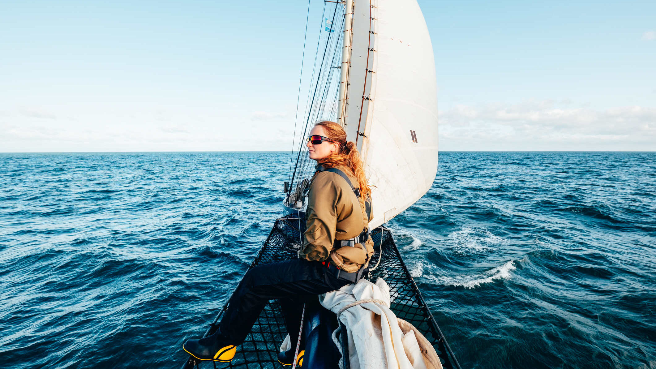 Woman sat on the bowsprit of a tall ship at sea