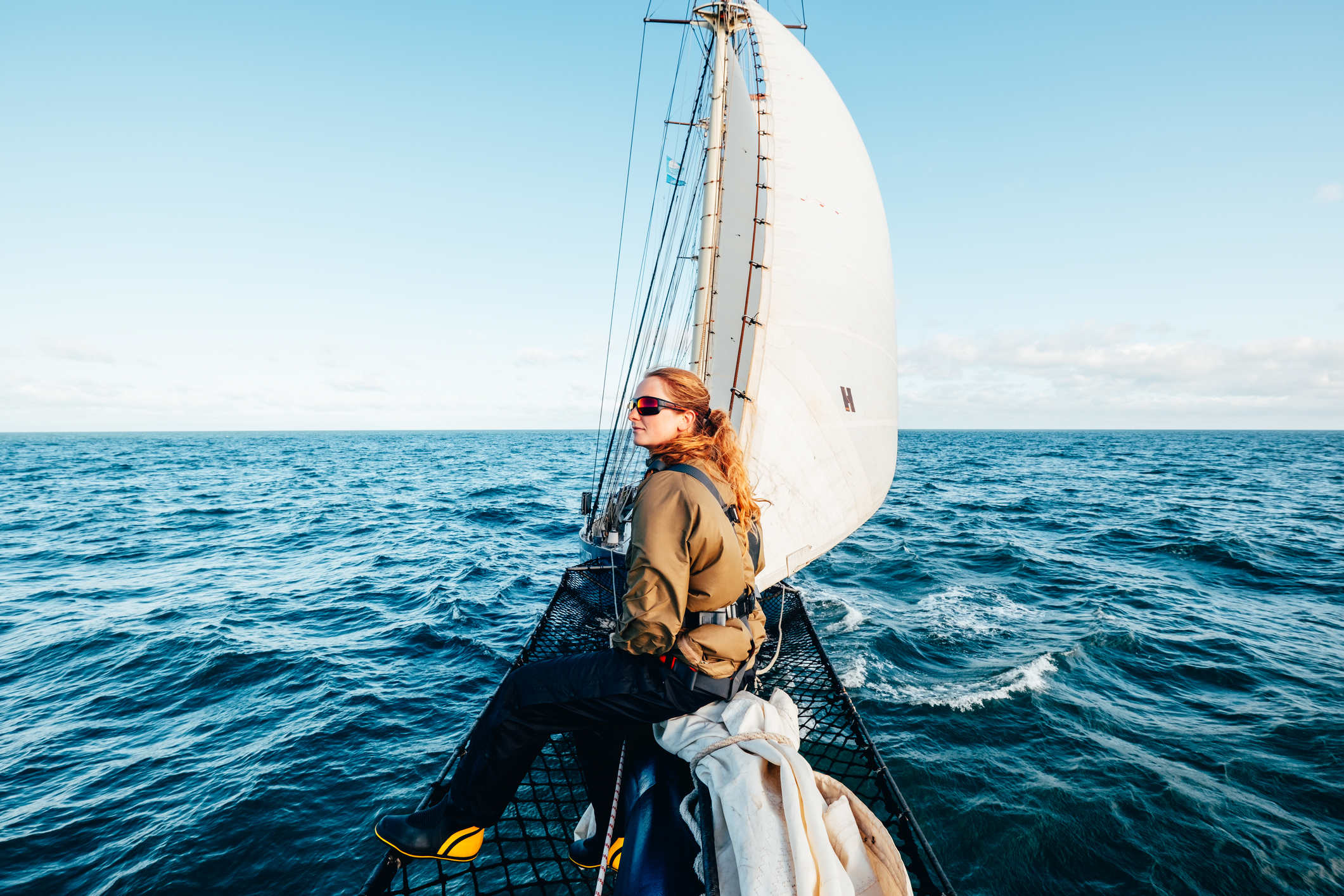 Woman sat on the bowsprit of a tall ship at sea