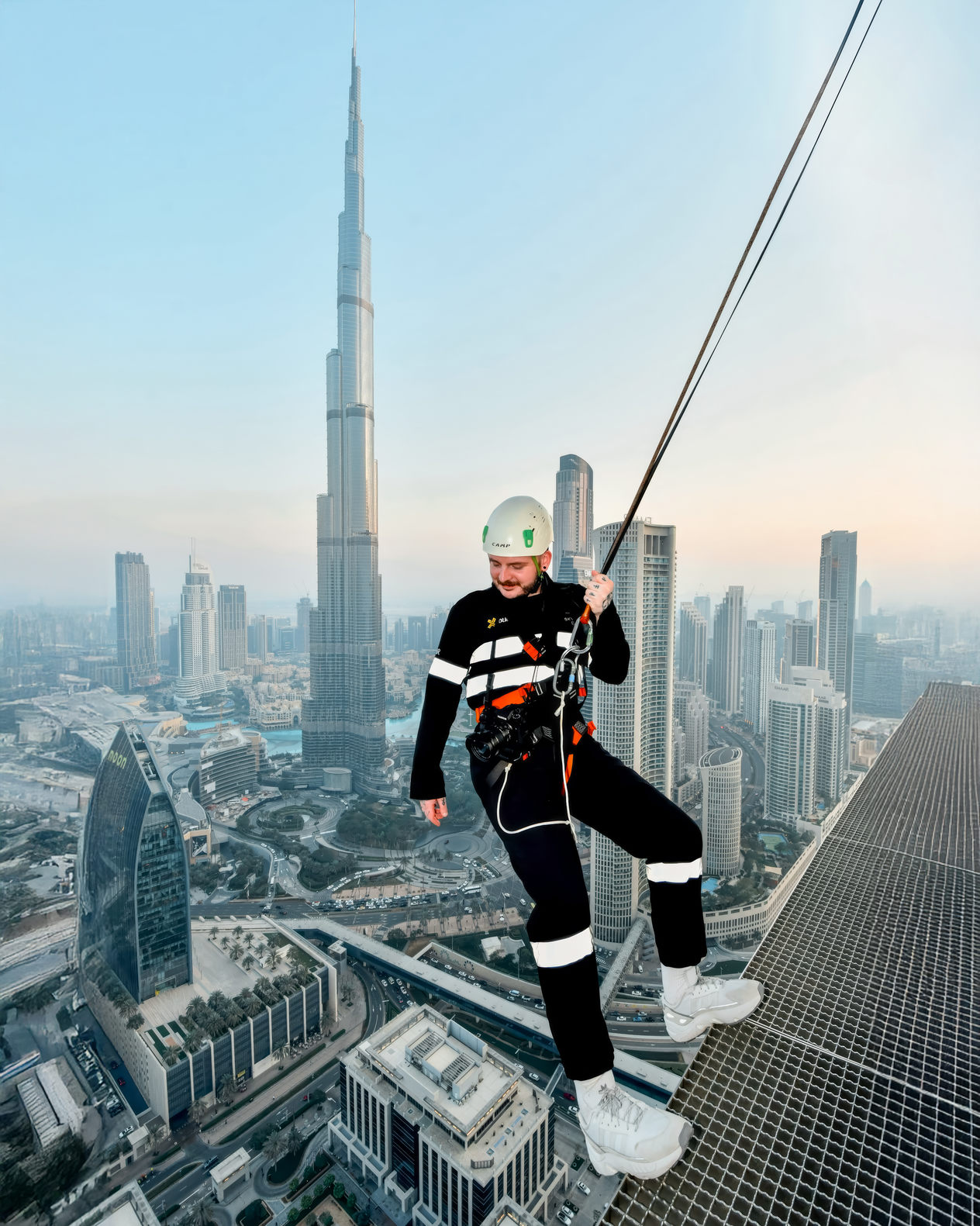 man hanging from a skyscraper with the Burj khalifa in background